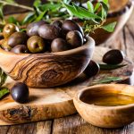 Olives and olive oil in olive wooden bowls on olive wooden cutting board, olive tree branch on wooden rustic background