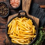 Skilet full of Potato french fries with salt. Wooden background. Top view.